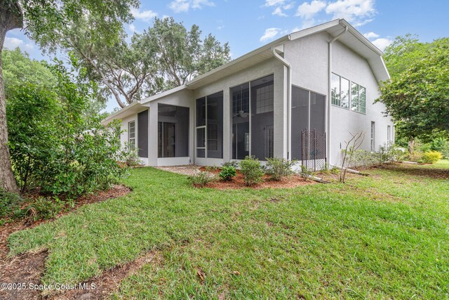 rear view of house featuring a sunroom, a yard, and stucco siding
