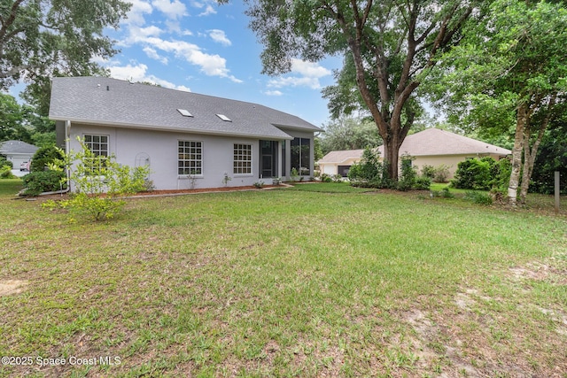 rear view of house featuring a lawn and stucco siding