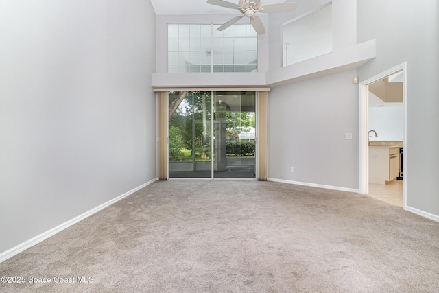 spare room featuring carpet floors, a high ceiling, ceiling fan, baseboards, and a sink