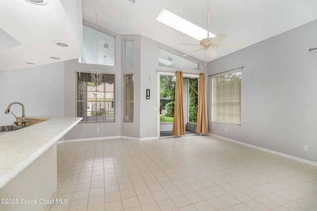 unfurnished living room with a ceiling fan, baseboards, a skylight, light tile patterned floors, and high vaulted ceiling