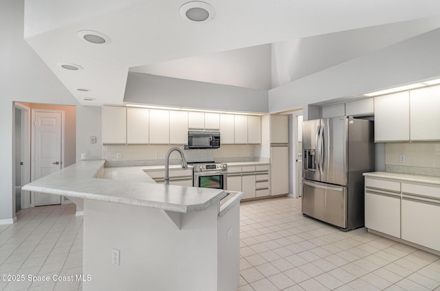 kitchen featuring appliances with stainless steel finishes, a peninsula, backsplash, a sink, and light tile patterned floors