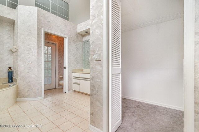 bathroom with toilet, vanity, tile patterned flooring, a bath, and baseboards
