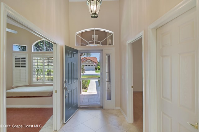 tiled foyer entrance with healthy amount of natural light, baseboards, a towering ceiling, and carpet flooring