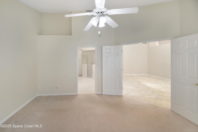 unfurnished room with a towering ceiling, light carpet, a ceiling fan, and baseboards