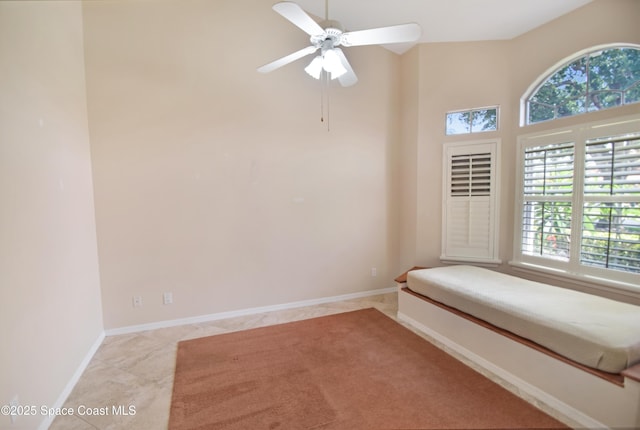 tiled empty room with healthy amount of natural light, ceiling fan, baseboards, and a high ceiling
