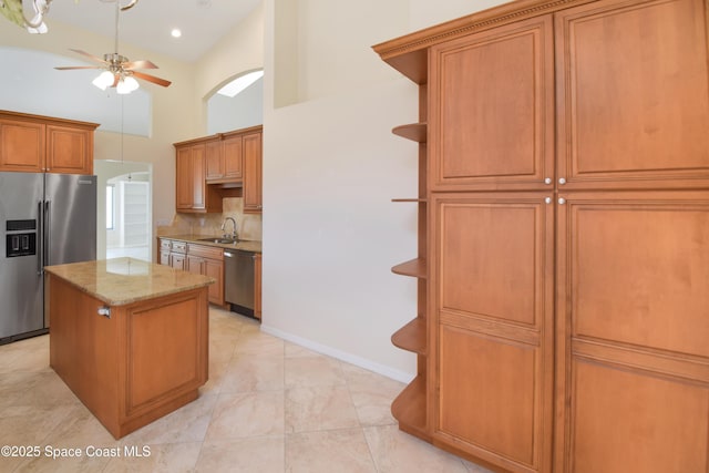kitchen featuring appliances with stainless steel finishes, a ceiling fan, a high ceiling, a sink, and a center island