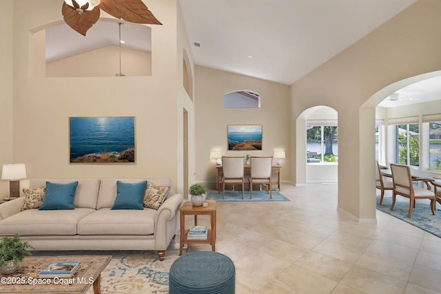 living area with high vaulted ceiling, light tile patterned floors, baseboards, arched walkways, and ceiling fan