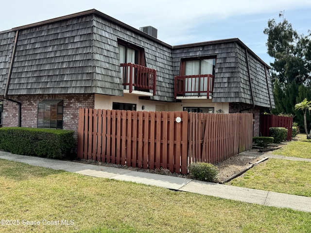 view of front of house featuring mansard roof, fence, a front yard, a balcony, and brick siding