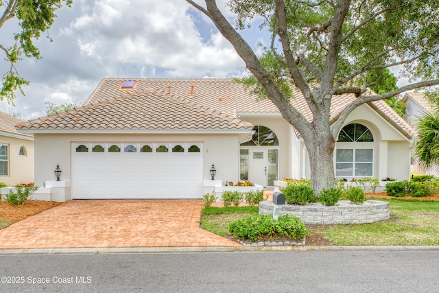 view of front of house featuring stucco siding, decorative driveway, a tiled roof, and a garage