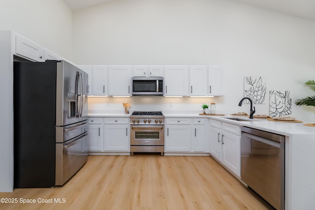 kitchen featuring stainless steel appliances, a sink, a towering ceiling, light countertops, and white cabinetry