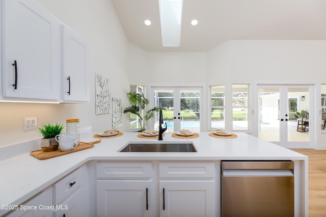 kitchen featuring french doors, stainless steel dishwasher, a sink, a peninsula, and light countertops