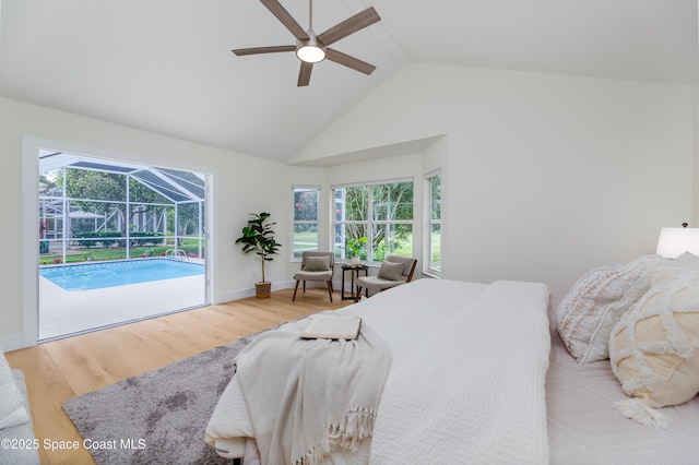 bedroom featuring a sunroom, access to exterior, wood finished floors, multiple windows, and high vaulted ceiling