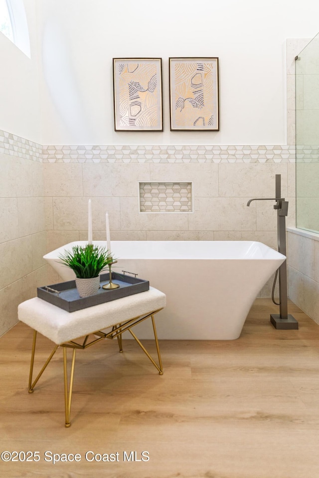 bathroom featuring tile walls, a freestanding bath, wood finished floors, and a wainscoted wall