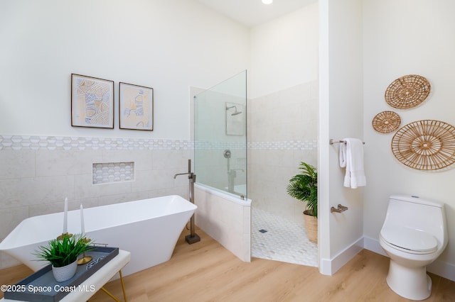 bathroom with tile walls, wood finished floors, a walk in shower, a freestanding bath, and toilet
