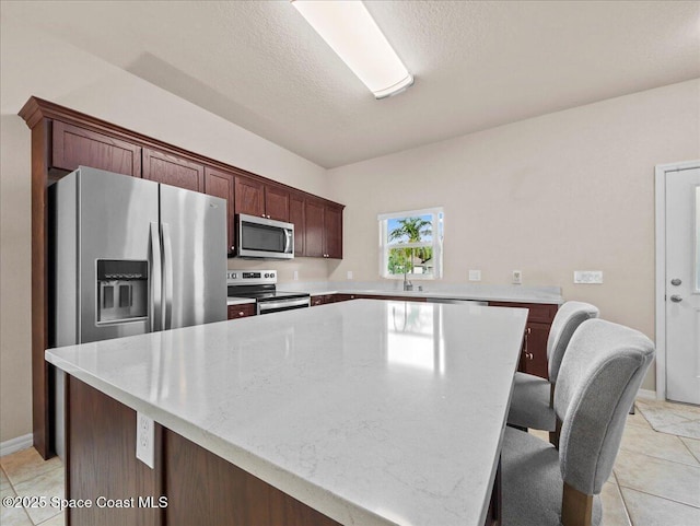 354 Dryden Cir, Cocoa, FL 32926 - kitchen featuring stainless steel appliances, light tile patterned floors, a center island, a textured ceiling, and a kitchen bar