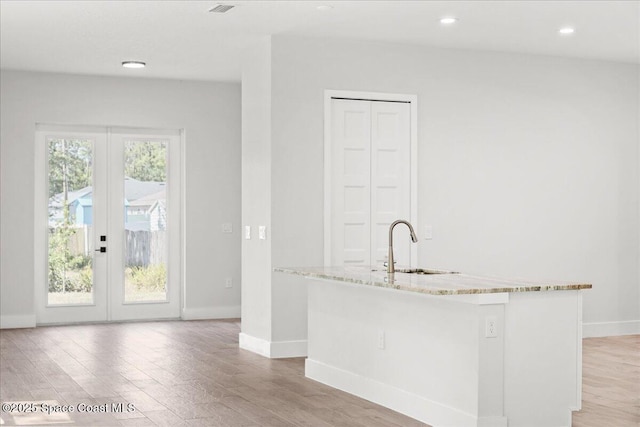 998 Wacona St SE, Palm Bay, FL 32909 - kitchen featuring french doors, light wood-type flooring, a sink, light stone countertops, and baseboards