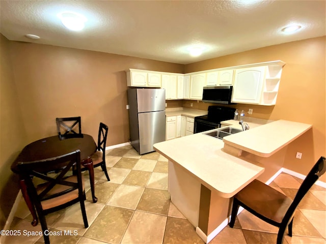kitchen featuring appliances with stainless steel finishes, a peninsula, a sink, a kitchen bar, and white cabinets