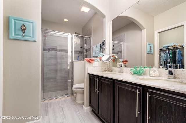 full bathroom with a shower stall, double vanity, toilet, and a walk in closet