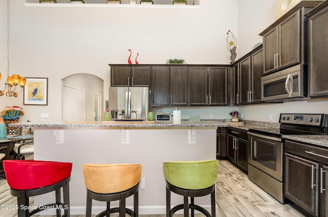 kitchen with appliances with stainless steel finishes, a breakfast bar, light wood finished floors, and dark brown cabinets