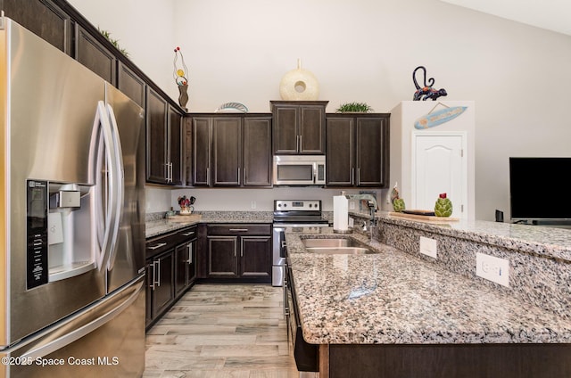 kitchen featuring stainless steel appliances, a sink, light wood-type flooring, and light stone counters