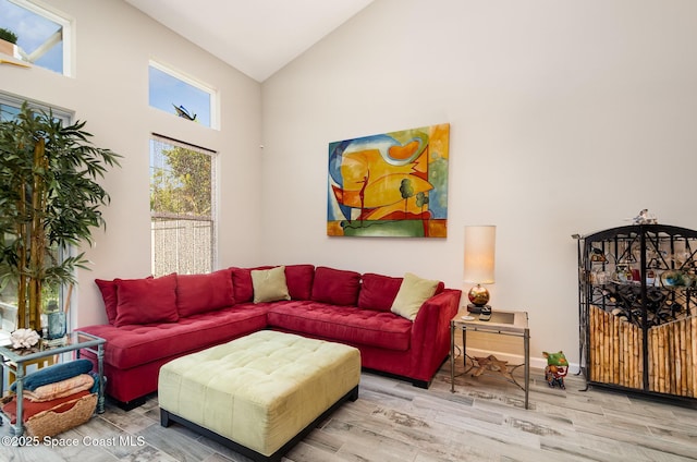 living area with high vaulted ceiling, healthy amount of natural light, and wood finished floors