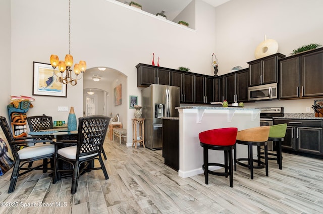kitchen featuring stainless steel appliances, a towering ceiling, arched walkways, a chandelier, and light wood-style floors