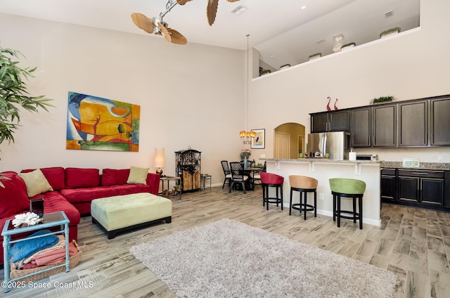 living area with light wood-style flooring, arched walkways, high vaulted ceiling, and baseboards