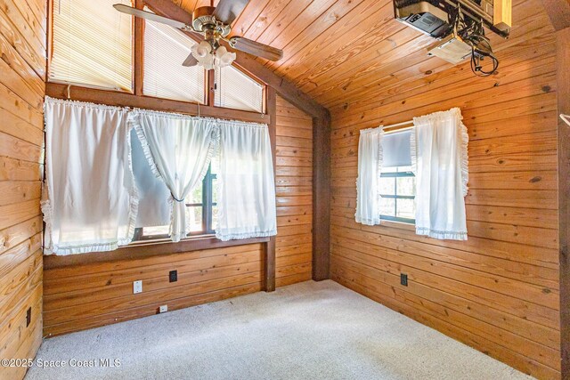 carpeted spare room featuring healthy amount of natural light, wood walls, vaulted ceiling, a ceiling fan, and wooden ceiling