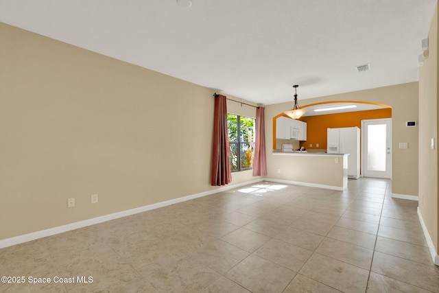 unfurnished living room with arched walkways, light tile patterned floors, and baseboards