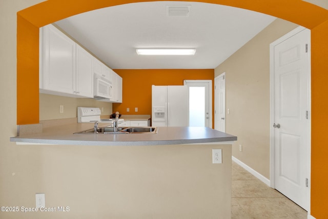 kitchen featuring white appliances, a peninsula, a sink, arched walkways, and light tile patterned floors