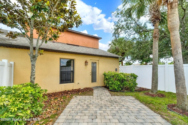 back of house featuring a patio area, stucco siding, fence, and roof with shingles