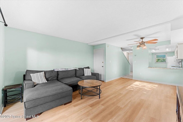 living area with light wood-style floors, ceiling fan, and baseboards