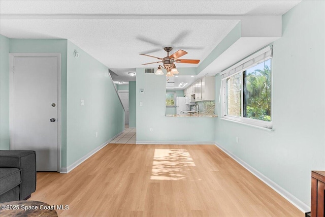 unfurnished room featuring light wood-type flooring, ceiling fan, baseboards, and a textured ceiling