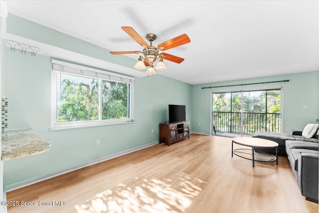 living area with light wood-style flooring, a ceiling fan, and baseboards