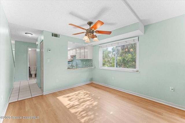 empty room featuring ceiling fan, light wood-style flooring, a sink, a textured ceiling, and baseboards