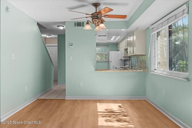 kitchen featuring freestanding refrigerator, ceiling fan, light wood finished floors, a sink, and a textured ceiling