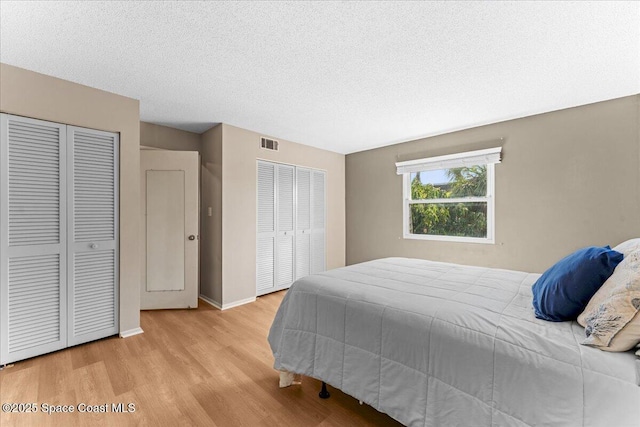 bedroom with multiple closets, wood finished floors, baseboards, and a textured ceiling