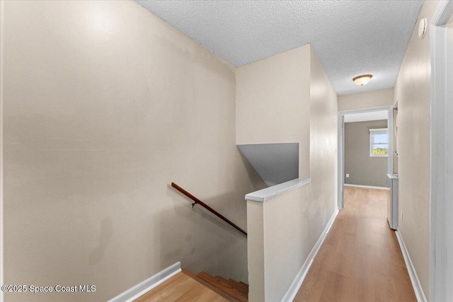 hallway with an upstairs landing, light wood-style floors, a textured ceiling, and baseboards
