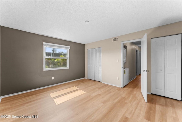 unfurnished bedroom with light wood-style floors, a textured ceiling, baseboards, and multiple closets