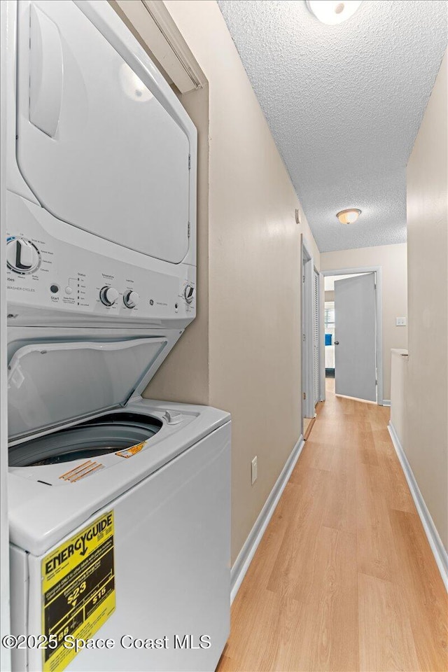laundry room with stacked washer / drying machine, light wood-style flooring, a textured ceiling, and baseboards