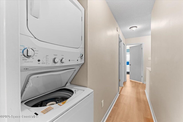 washroom featuring stacked washer / drying machine, light wood-type flooring, a textured ceiling, and baseboards