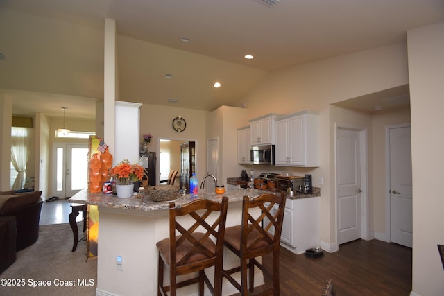 kitchen with stainless steel microwave, a breakfast bar, dark wood-style flooring, white cabinets, and lofted ceiling