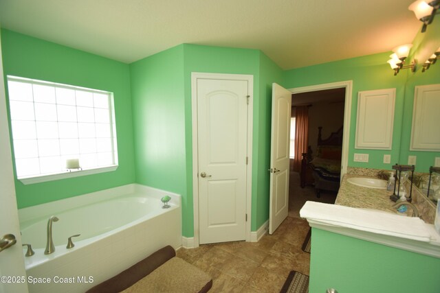 ensuite bathroom with a garden tub, vanity, and baseboards