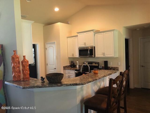 kitchen featuring stainless steel appliances, lofted ceiling, a peninsula, dark stone counters, and white cabinetry