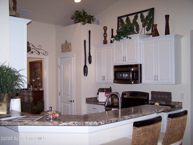 kitchen with appliances with stainless steel finishes, white cabinetry, a peninsula, dark stone countertops, and recessed lighting