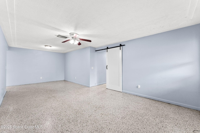 unfurnished room featuring a ceiling fan, speckle patterned floor, a barn door, baseboards, and a textured ceiling