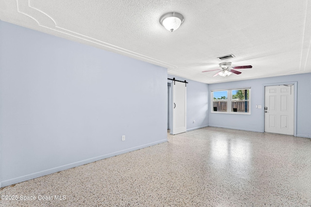 unfurnished room featuring a textured ceiling, ceiling fan, a barn door, speckle patterned floor, and baseboards