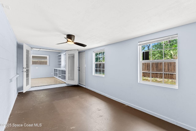 unfurnished room with concrete flooring, baseboards, a ceiling fan, and plenty of natural light