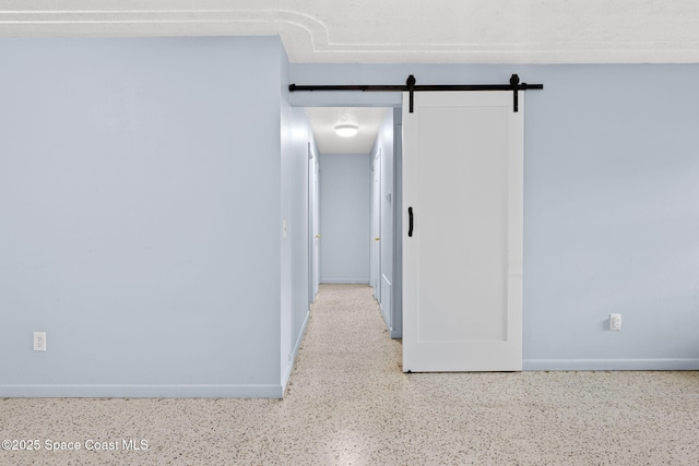 hall with speckled floor, baseboards, and a barn door