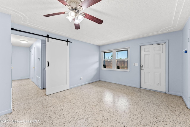 unfurnished living room featuring a textured ceiling, a barn door, speckle patterned floor, ceiling fan, and baseboards